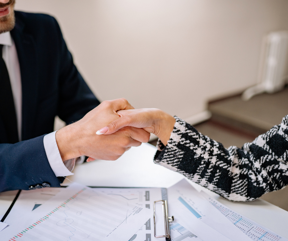 Financial advisor shaking hands with client over desk covered with charts and documents, representing professional consultation about life insurance policy loans