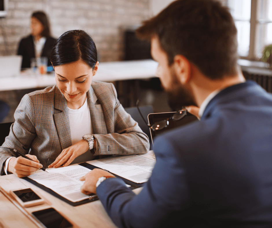 Woman in plaid blazer signing financial documents during consultation meeting with advisor, representing the process of securing a policy-backed loan