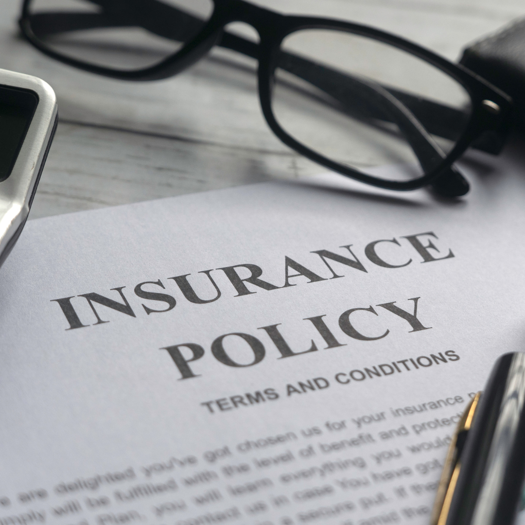 A printed insurance policy terms and conditions document on a marble surface, with a black-framed pair of glasses, a pen, and a smartphone nearby.